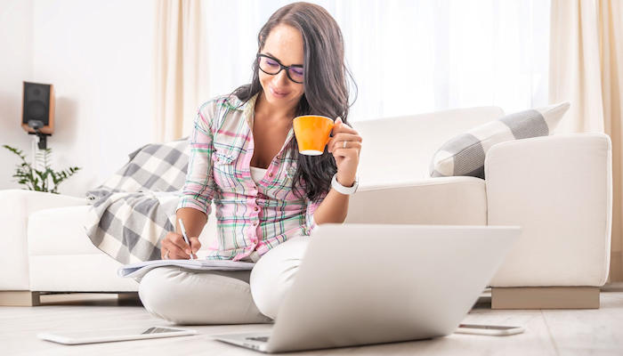 Eine am Boden sitzende Frau mit Laptop und Kaffee